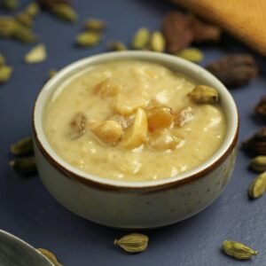 A bowl of traditional Indian kheer garnished with nuts and cardamom on a dark background.