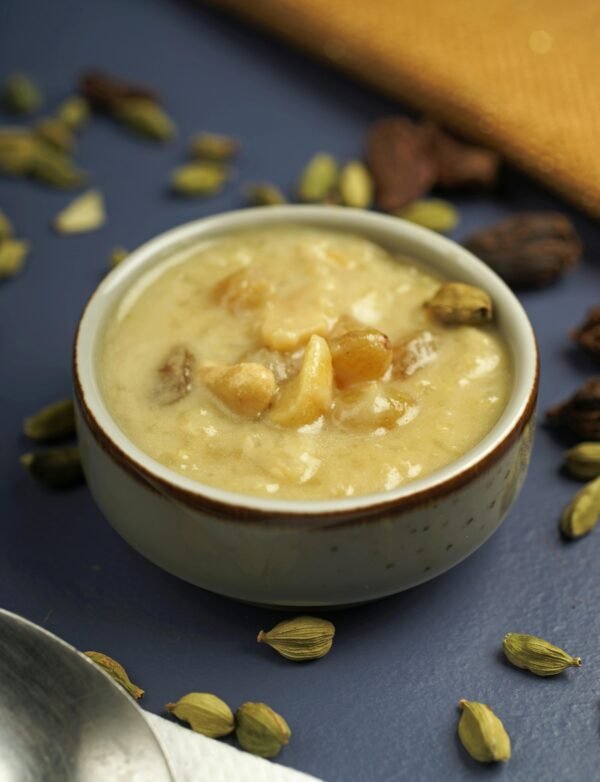 A bowl of traditional Indian kheer garnished with nuts and cardamom on a dark background.