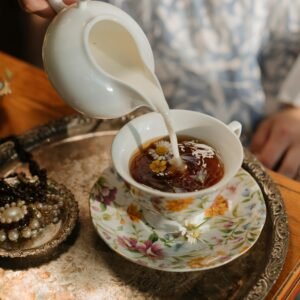 A vintage tea scene with milk being poured into chamomile tea, surrounded by pearls and ornate jewelry.